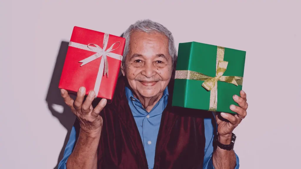 A smiling senior Indian woman unwrapping a thoughtful gift surrounded by family, inspired by Samarth Eldercare's guide to the best gifts for ageing parents in India