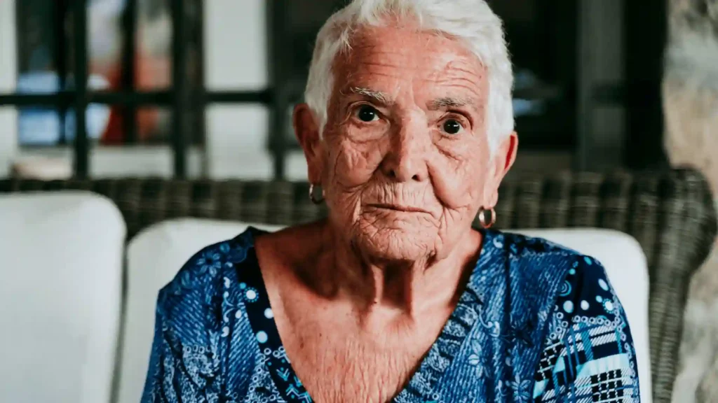 An elderly couple seated in a comfortable old-age home common room — Samarth Eldercare weighs the advantages and disadvantages of community living versus staying at home