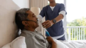 A caregiver gently repositioning a bedridden elderly person on a clean bed, representing Samarth Eldercare's compassionate guide to at-home care for immobile seniors