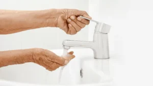 A caregiver assisting an elderly man with grooming — combing hair and washing hands — showing Samarth Eldercare's respectful personal hygiene support guide