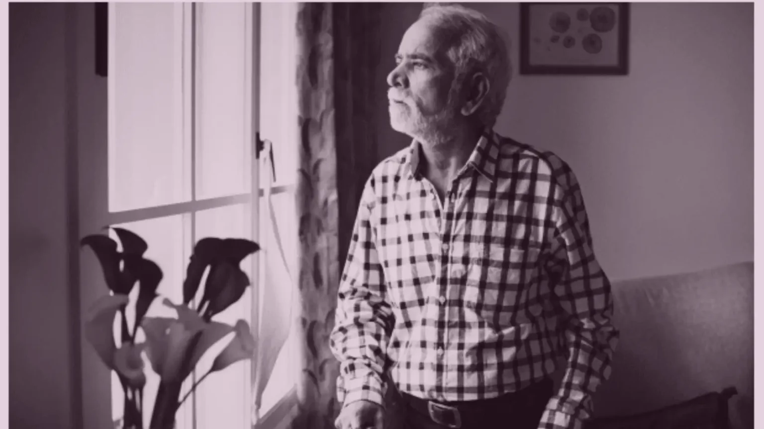 An elderly person sitting alone at home by a window, looking out quietly