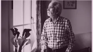 An elderly person sitting alone at home by a window, looking out quietly