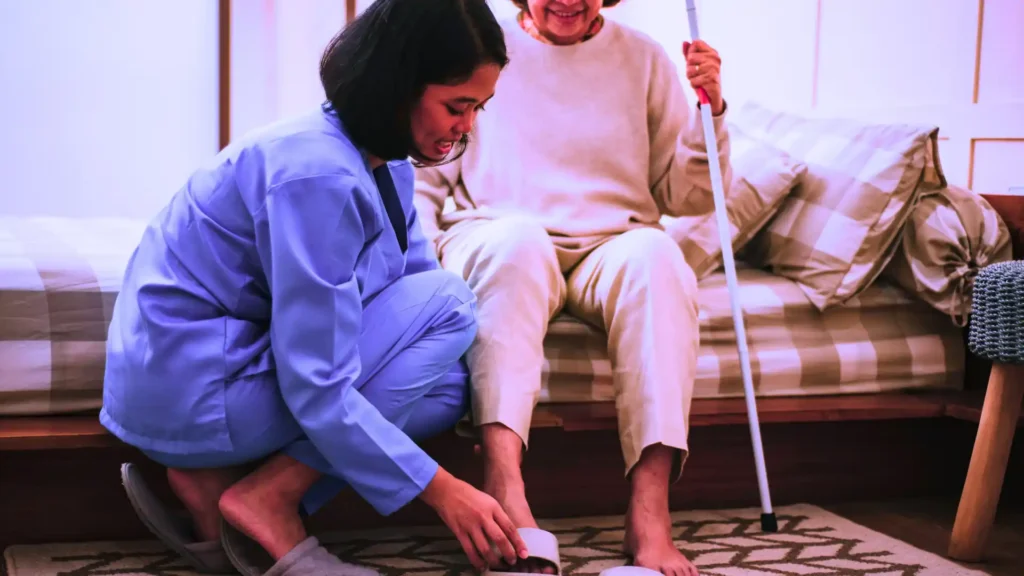 Trained caregiver providing physical assistance for elderly at home in India
